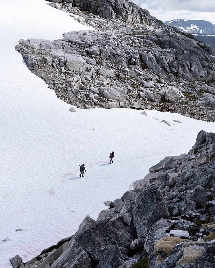 Two hunters cross a snowy pass between rock formations while mountain hunting.